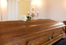 A wooden casket with a white rose placed on top in a solemn setting
