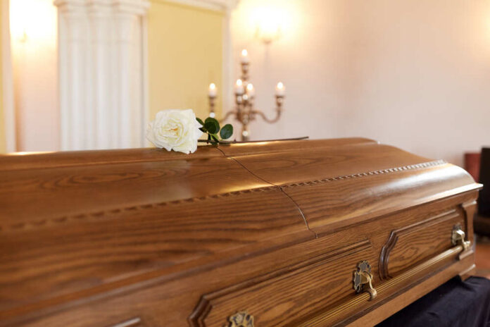 A wooden casket with a white rose placed on top in a solemn setting