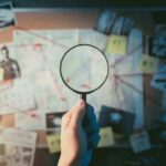 Hand holding magnifying glass over crime investigation evidence board.