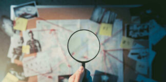 Hand holding magnifying glass over crime investigation evidence board.