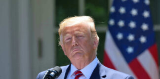 Donald Trump speaking with US flag in the back.