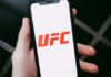 A hand holding a smartphone displaying the UFC logo