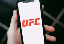 A hand holding a smartphone displaying the UFC logo