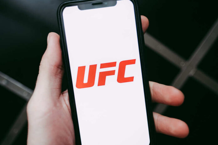 A hand holding a smartphone displaying the UFC logo