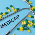 A stethoscope placed on a blue background with green and yellow capsules and the word 'Medigap'