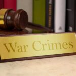 A wooden gavel next to a nameplate reading 'War Crimes'