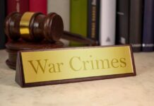 A wooden gavel next to a nameplate reading 'War Crimes'