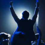 Silhouetted person with raised fists at a lit event.