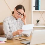 Woman in a home office reading a document with a focused expression