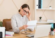 Woman in a home office reading a document with a focused expression