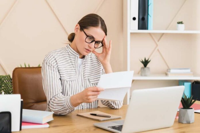 Woman in a home office reading a document with a focused expression