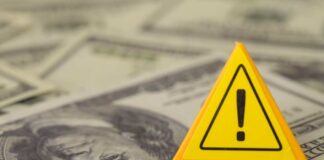 A yellow warning sign placed on a background of dollar bills