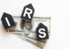 Blocks spelling 'IRS' placed on top of hundred dollar bills featuring Benjamin Franklin