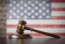 A wooden gavel resting on a sound block with an American flag background