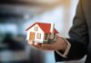A person holding a small model house in a business setting