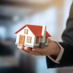 A person holding a small model house in a business setting