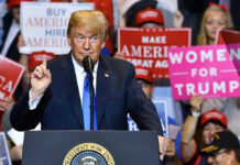 Man speaking at podium with various political signs behind.