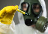 Person in protective gear holding a test tube labeled 'VIRUS'