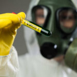 Person in protective gear holding a test tube labeled 'VIRUS'
