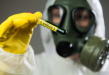 Person in protective gear holding a test tube labeled 'VIRUS'