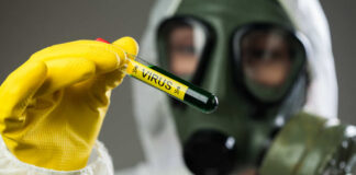 Person in protective gear holding a test tube labeled 'VIRUS'