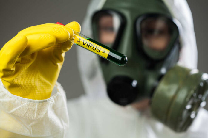 Person in protective gear holding a test tube labeled 'VIRUS'