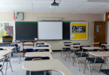 Empty classroom with desks, projector, and chalkboard.