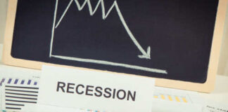 A sign reading 'RECESSION' in front of various financial charts and a downward trend graph