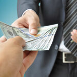 Shocking $1K Payments Hit Hard-Working Americans Hard A person handing over a stack of cash to another individual in a suit