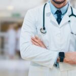 A doctor in a white coat with a stethoscope standing with arms crossed