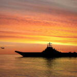 Boat War Escalates — Proof Still Missing? Silhouette of an aircraft carrier at sunset.