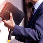 MAGA Pastor’s Run EXPLODES Over Flirty Texts Man holding a Bible during a speech or presentation.