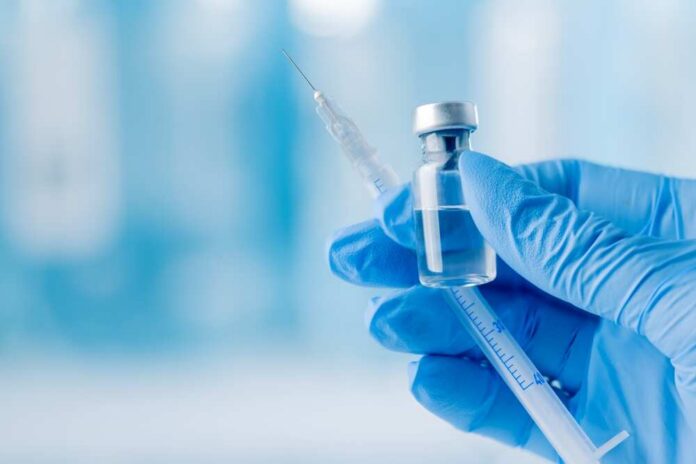A gloved hand holding a syringe and a vial of liquid