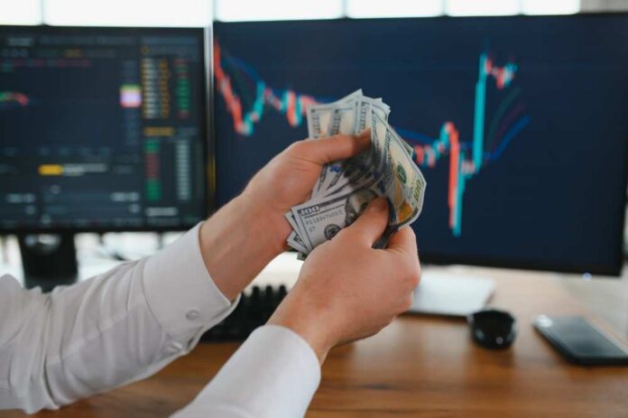 Holding,Dollar,Bills,In,The,Stock,Market.,Investors,Counting,Money Person holding cash in front of stock market charts on computer screens