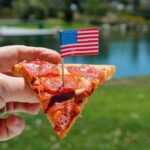Pepperoni pizza slice on a paper plate over an American flag