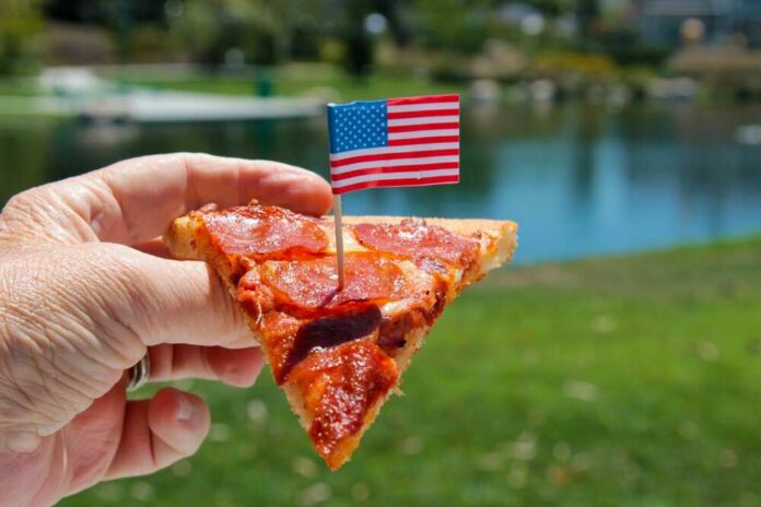 Pepperoni pizza slice on a paper plate over an American flag