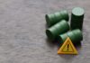 Four green barrels and a warning sign on a wooden surface