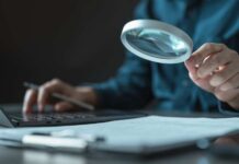 Person using a magnifying glass while working on a laptop