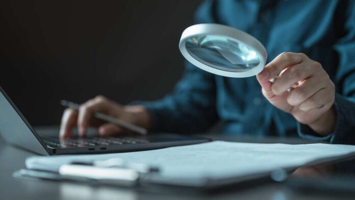 Person using a magnifying glass while working on a laptop