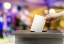 Hand placing ballot in voting box.