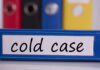 Blue binder labeled 'cold case' with other colored binders in the background