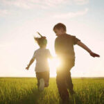 Children running in a field at sunset.