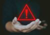 A hand holding a red warning triangle with an exclamation mark