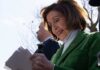 Nancy Pelosi smiling while holding papers outdoors