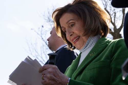 Nancy Pelosi smiling while holding papers outdoors