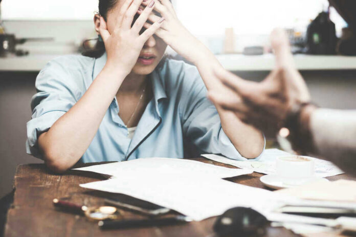 Stressed woman with hands on face at a desk.