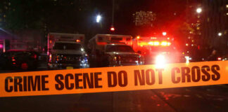 Crime scene tape with emergency vehicles in background.