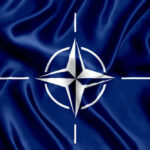NATO flag with white compass emblem on blue background.