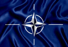 NATO flag with white compass emblem on blue background.