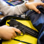 Kid placing handgun inside a backpack on desk